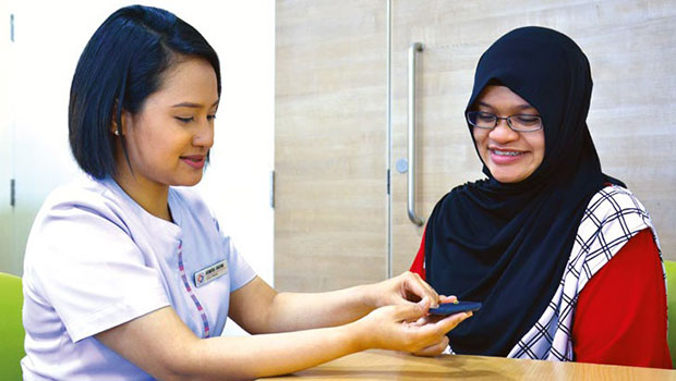 Asmira Bte Mohamed Rahim, guides a pregnant patient on the self-administered finger-prick test to monitor her blood sugar levels.